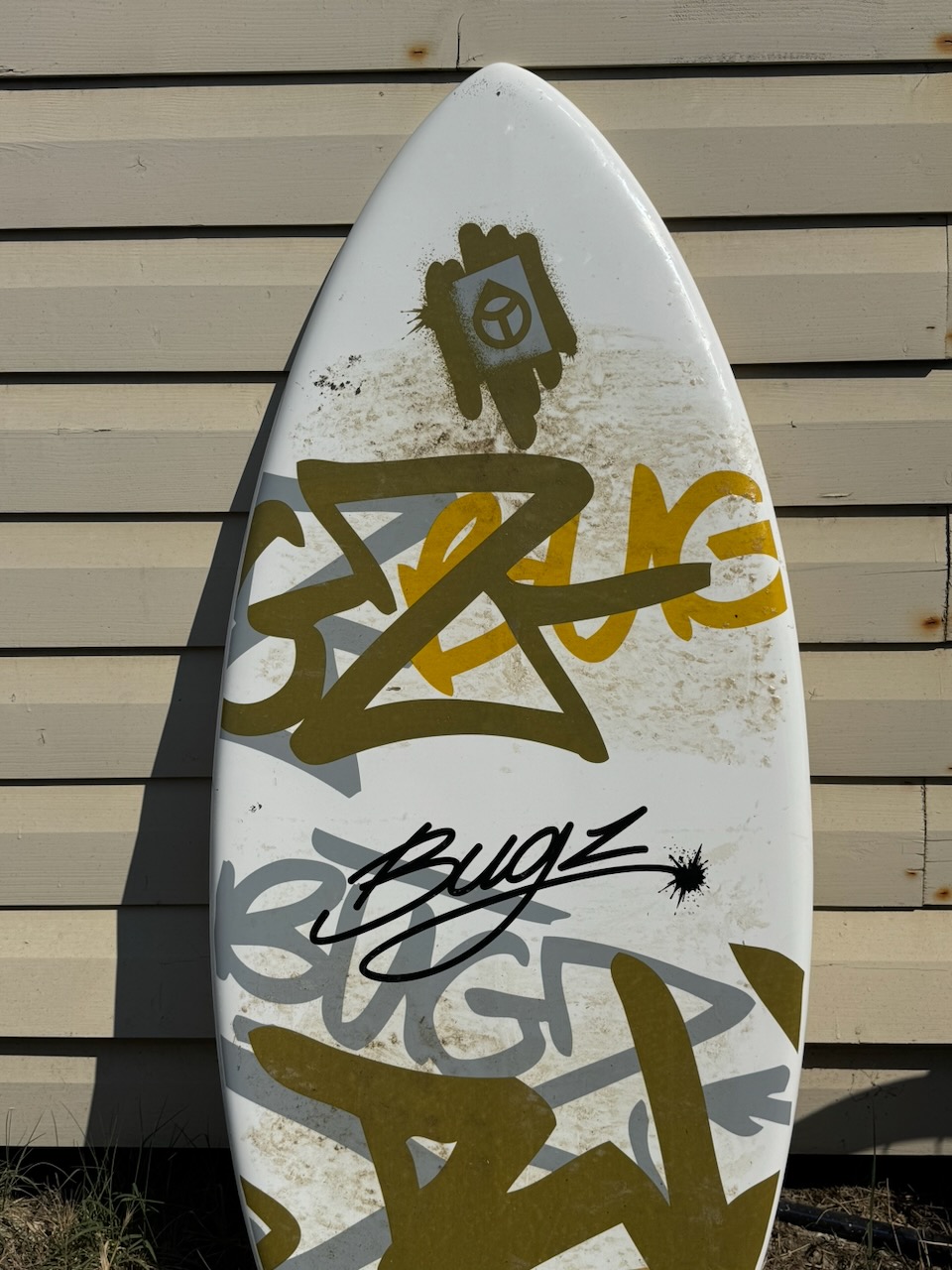 A graffiti-covered surfboard leaning against a weathered wall
